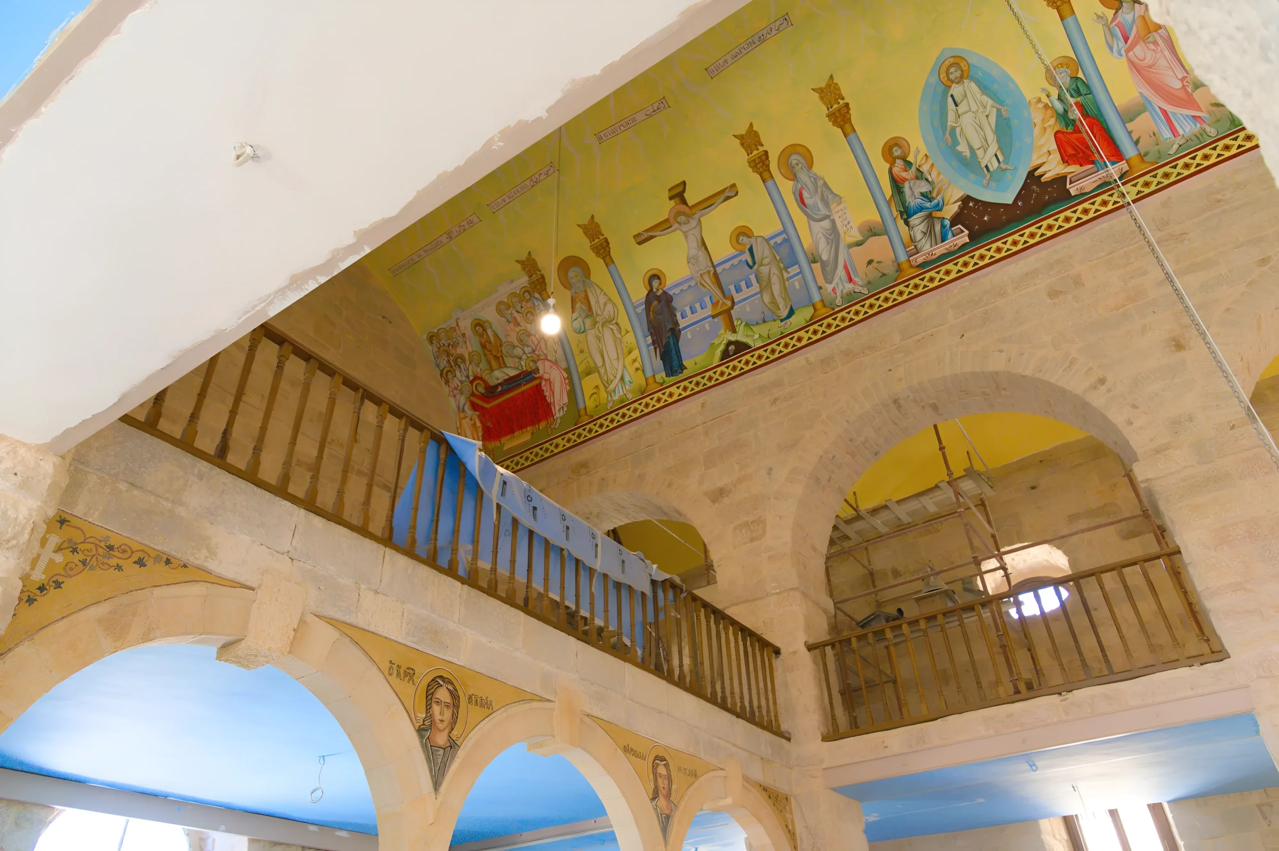 Partie intérieure d'une église orthodoxe ancienne avec fresques religieuses et architecture en pierre, en cours de restauration avec une bâche bleue visible