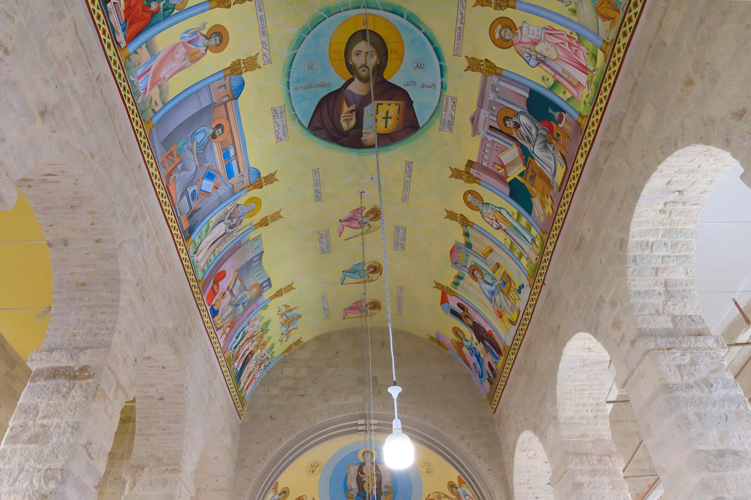 Plafond de l’église Saint-Georges à Madaba avec fresques colorées, figure centrale du Christ, murs en pierre beige et arches, éclairage chaud