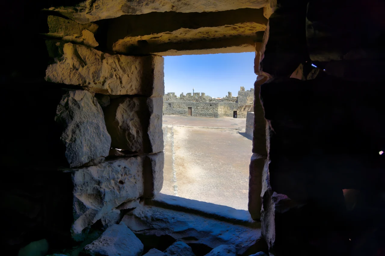 Embrasure de porte en pierre ouvrant sur cour désertique avec structures calcaires anciennes