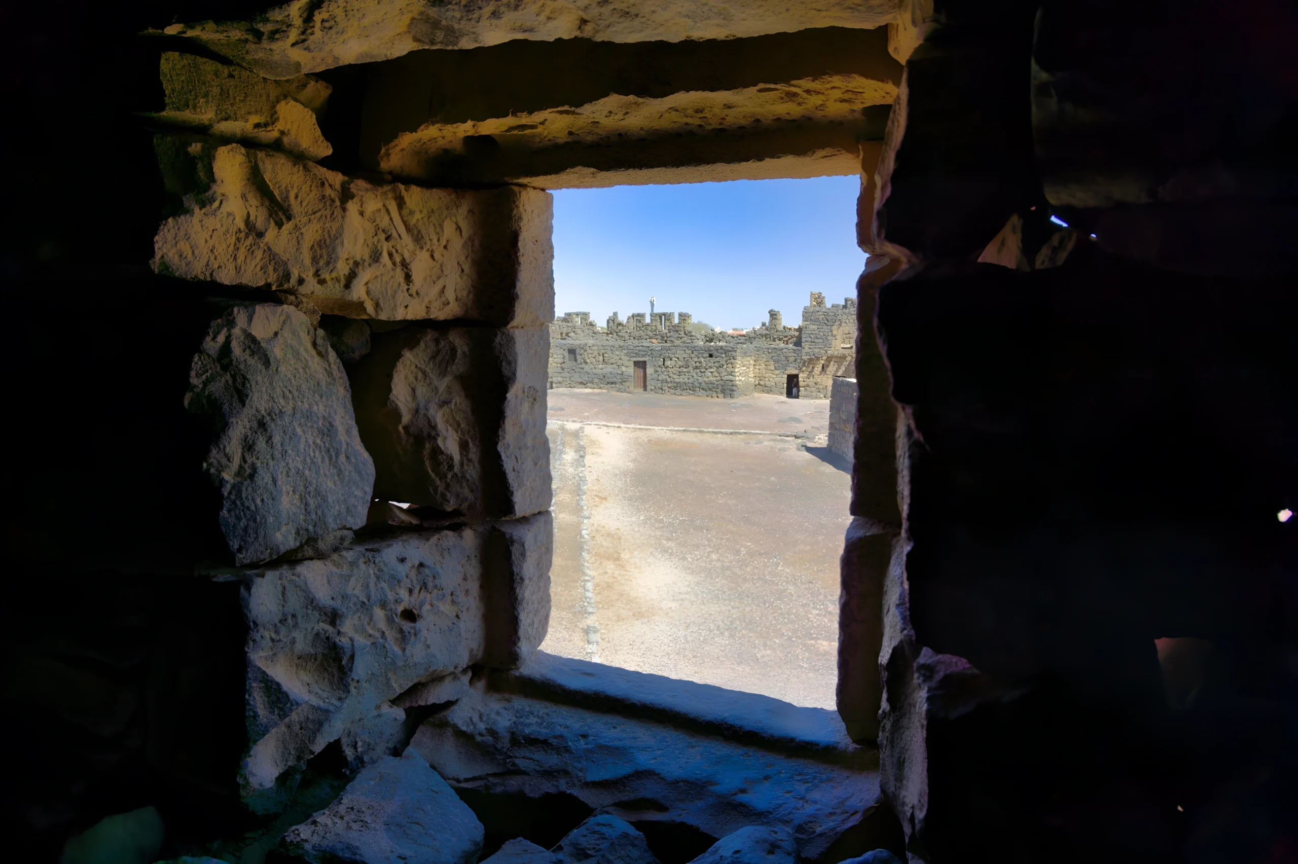 Embrasure de porte en pierre ouvrant sur cour désertique avec structures calcaires anciennes