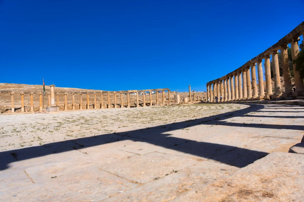 Colonnes dorées alignées sur sol dallé sous ciel bleu dans paysage désertique antique